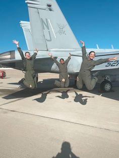 three people are posing in front of an airplane on the tarmac with their hands up