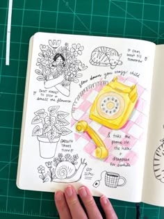 a hand is holding an open notebook with drawings on it and a phone in the middle