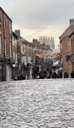 an old cobblestone street with people walking on the sidewalk and buildings in the background