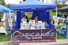 some people are standing at a booth selling cupcakes