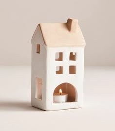 a small white house shaped candle holder with a lit candle in the front and side