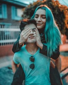 a woman covering her eyes while standing next to a man with blue hair and wearing a black jacket