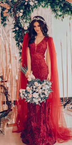 a woman in a red dress holding a bouquet and wearing a veil over her head