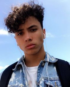 a young man with earphones on his ears looking at the camera while wearing a denim jacket and white t - shirt