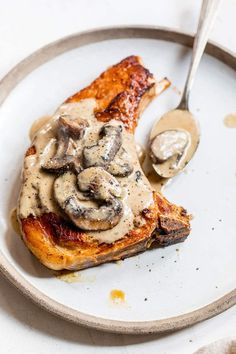 a white plate topped with meat covered in mushroom gravy next to a spoon