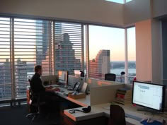 a man sitting at a desk in an office with two computer monitors and a laptop