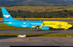 a blue and yellow plane is on the runway at an airport with mountains in the background