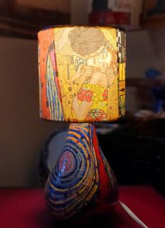 a lamp that is sitting on top of a red table with a painting on it