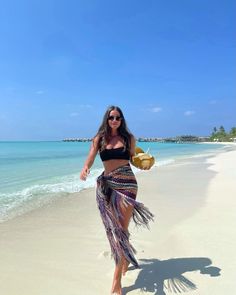 a woman is walking on the beach wearing a skirt