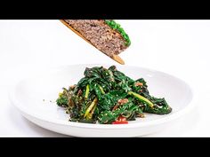 a white plate topped with green vegetables and a slice of bread on top of it