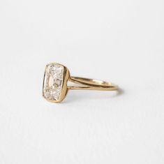 a yellow gold engagement ring with a square cut diamond in the center, on a white background