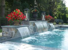 an outdoor pool with waterfall and red flowers