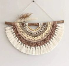 a white wall hanging with fringes and beads on the bottom, next to a wooden stick