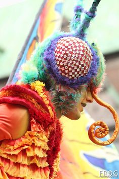 a person with colorful hair and headdress standing next to a pole