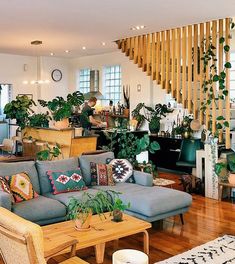 a living room filled with lots of furniture and plants on top of wooden floors next to a stair case