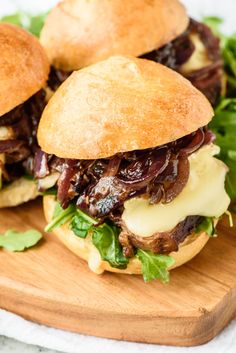 two sandwiches with meat, cheese and lettuce on a cutting board