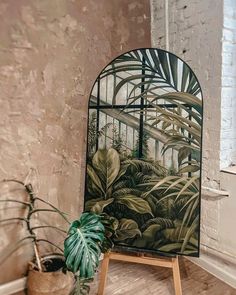 a painting on an easel next to a potted plant in a room with brick walls