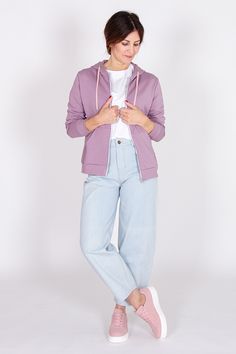 a woman standing in front of a white background wearing a purple jacket and light blue jeans