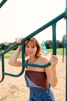 a woman in overalls holding onto the bars of a playground