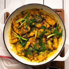 a pan filled with chicken and vegetables on top of a wooden cutting board