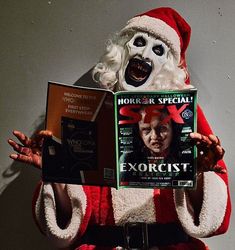 a man in a santa suit holding up a magazine with an evil face on it