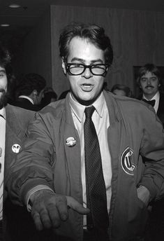 black and white photograph of two men in suits with badges on their jackets, one pointing at the camera