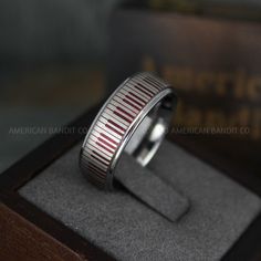 a silver ring with red and white stripes on it in a wooden box, next to a book