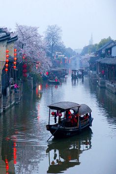 a boat with people on it traveling down a river surrounded by buildings and lanterns in the sky