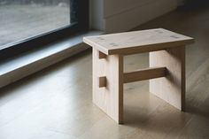 a small wooden stool sitting on top of a hard wood floor next to a window