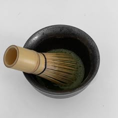 a wooden whisk in a black bowl on a white surface