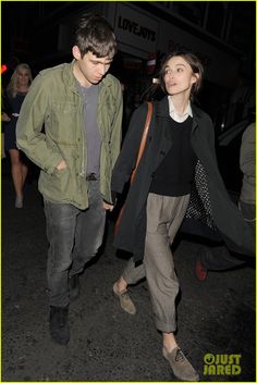 a young man and woman walking down the street at night with their hands in each other's pockets