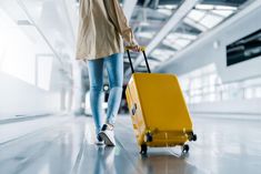 a woman is pulling a yellow suitcase down the hall way in an airport or terminal