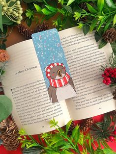 an open book with a bear on it surrounded by evergreen leaves and pine cones,