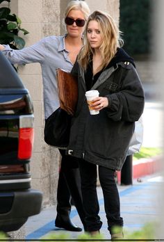 two women standing next to each other on the sidewalk with drinks in hand and one holding a coffee cup