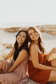 two young women sitting on the beach smiling at the camera and posing for a photo