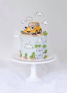 a birthday cake with a yellow car on top and clouds in the sky behind it