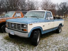 two pickup trucks parked next to each other on a field covered in snow and ice