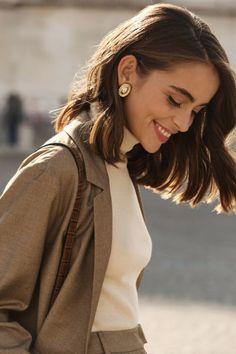 a woman with long hair is looking down at her cell phone while wearing a tan coat