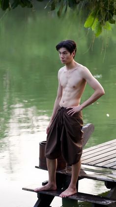 a shirtless man standing on a dock next to water