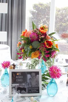 the table is set with vases, flowers and an empty photo frame on it