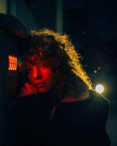 a woman with curly hair standing in front of a parking meter at night, looking off to the side