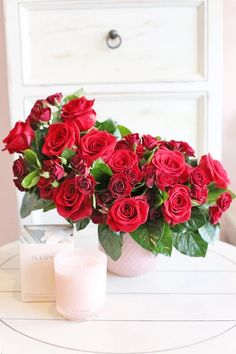 a vase filled with red roses next to a candle