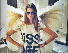 a woman with angel wings standing in front of a window wearing a t - shirt