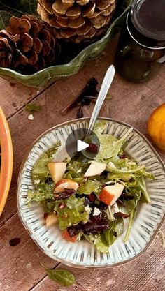 a salad with apples and cranberries in a bowl on a table next to pine cones