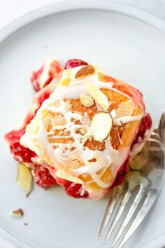 a white plate topped with fruit covered in icing and nuts next to a fork