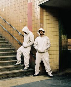 two men in white sweatsuits standing next to each other on the side of stairs