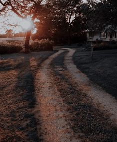 the sun shines brightly through the trees in front of a house on a dirt road