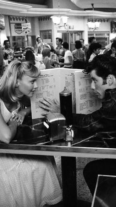 two people sitting at a table in a restaurant looking at each other's menus