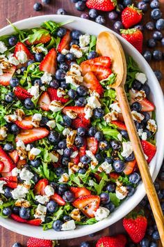 a salad with strawberries, blueberries and feta cheese in a white bowl