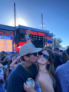 a man and woman kissing in front of a crowd at an outdoor music festival with the lights on